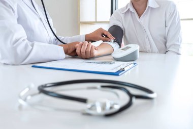 Doctor using stethoscope checking measuring arterial blood pressure on arm to a patient in the hospital, healthcare and medical concept.