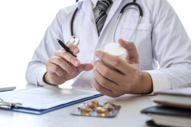 Hastane ve tıbbi steteskopta çalışan ve kağıt üzerinde yazan doktor. Masanın üzerinde duran ilaç..