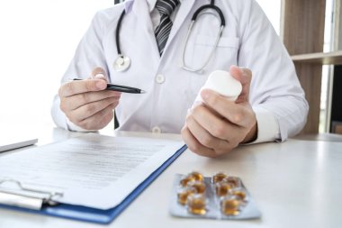 Hastane ve tıbbi steteskopta çalışan ve kağıt üzerinde yazan doktor. Masanın üzerinde duran ilaç..