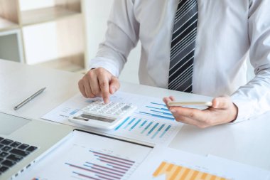 Bilgisayarda grafik üzerinde çalışan genç iş adamı ya da muhasebeci, veri istatistiklerini ve hesap makinesini analiz ederek pazarlama araştırma planlama raporunu sunar..