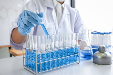 Laboratuvarda virüs ve aşı antiretroviral koronavirüs hakkında çalışan kadın araştırmacı ya da doktor test tüpleri ve mavi sıvı çözeltisi ile araştırma yapıyor..