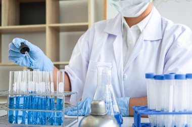 Laboratuvarda virüs ve aşı antiretroviral koronavirüs hakkında çalışan kadın araştırmacı ya da doktor test tüpleri ve mavi sıvı çözeltisi ile araştırma yapıyor..