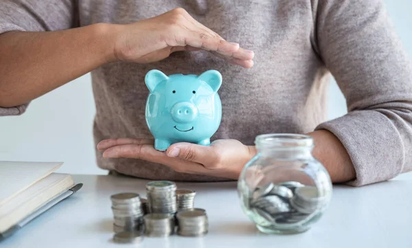 Young woman hands protection piggy bank and planning growing saving to strategy with pile coins for future plan fund of travel, education, home and retirement.