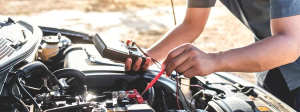 Otomatik onarım servisinde motor otomotiv kontrolü yapan tamirci ve çeşitli değerleri ölçmek ve analiz etmek için dijital çoklu metre test pili kullanıyor.
