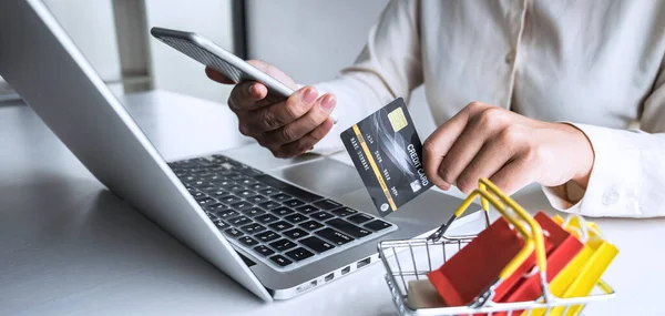 Business woman using smartphone, laptop and holding credit card for paying detail page display online shopping purchase and entry security code to inputting card information.