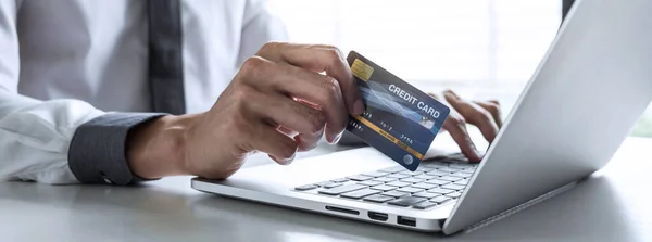 Businessman using laptop and holding credit card for paying detail page display online shopping purchase and entry security code to inputting card information.