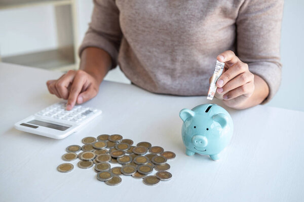 Young woman putting money into piggy bank planning growing saving to strategy and calculating with money box for future plan fund of travel, education, home and retirement.