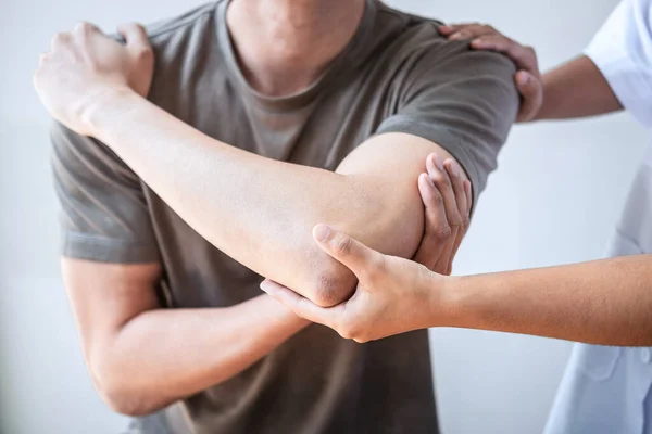 Kadın fizyoterapist, erkek sporcunun yaralı kolunu tedavi ediyor, esneme ve egzersiz yapıyor, klinikte rehabilitasyon tedavisi uyguluyor..