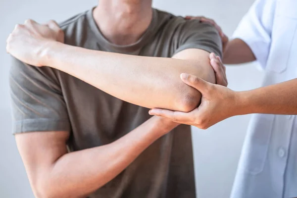 Doktor ya da fizyoterapist, sporcu erkek hastaların yaralı kollarını tedavi ediyor, esneme ve egzersiz yapıyor, klinikte rehabilitasyon tedavisi uyguluyor..