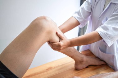Doktor ya da fizyoterapist, yaralı erkek hasta bacağını tedavi ediyor, klinikte rehabilitasyon tedavisi uyguluyor..