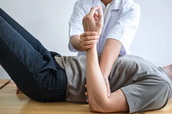 Doktor ya da fizyoterapist, sporcu erkek hastaların yaralı kollarını tedavi ediyor, esneme ve egzersiz yapıyor, klinikte rehabilitasyon tedavisi uyguluyor..