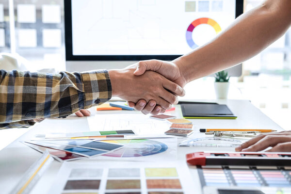 Team of young Interior graphic designer shaking hands after working sketching on color swatch, discussing of house project at modern office, creative work place inspiration and imagine.