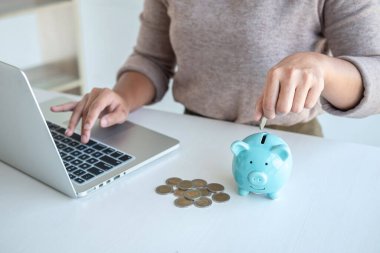 Genç kadın, gelecekte seyahat, eğitim, ev ve emeklilik fonu için para kutusu ile strateji oluşturmak amacıyla domuzcuk banka planlamasına madeni para koyuyor..