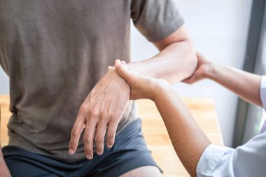 Kadın fizyoterapist, erkek sporcunun yaralı kolunu tedavi ediyor, esneme ve egzersiz yapıyor, klinikte rehabilitasyon tedavisi uyguluyor..