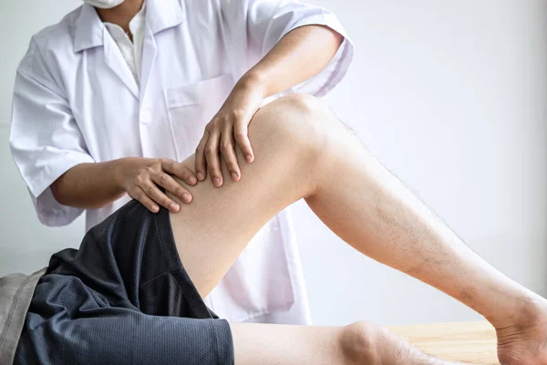 医師または理学療法士は 運動選手の男性患者の負傷脚の治療を検討作業 診療所でリハビリ療法の痛みを行う — ストック写真
