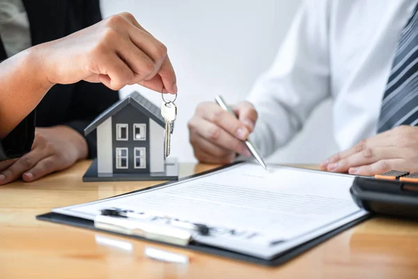 Home Insurance and Real estate investment concept, Sale agent giving house key to new client after signing agreement contract with approved property application form.