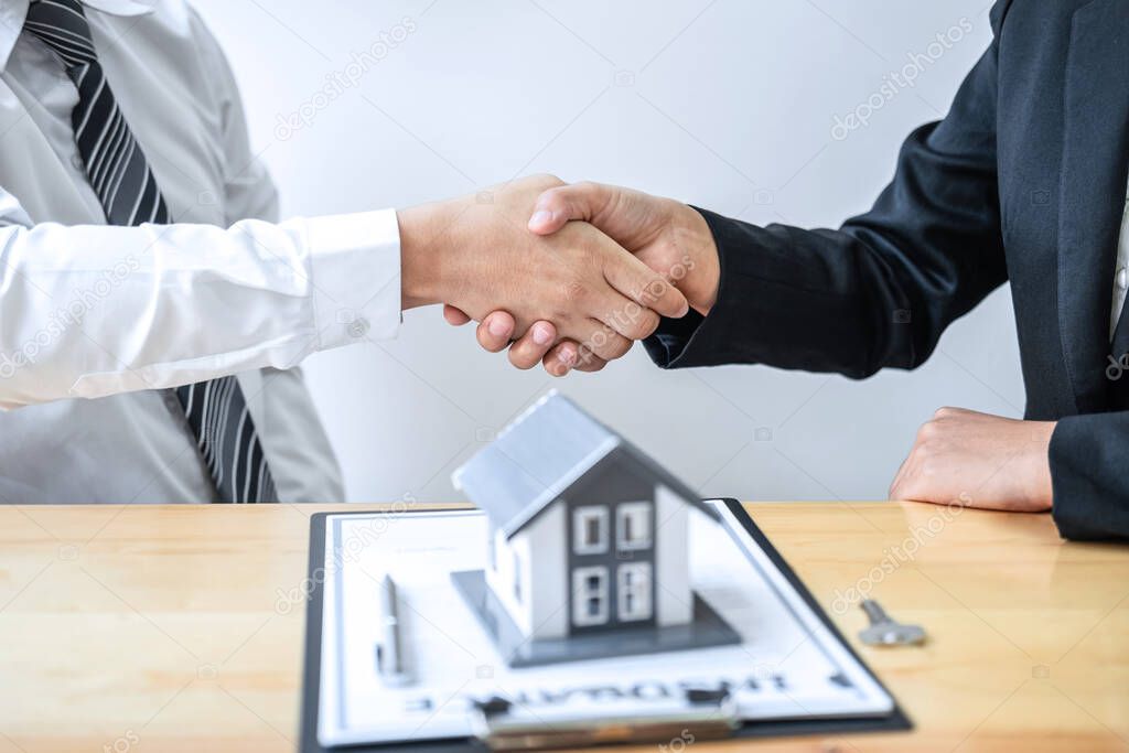 Real estate agent are shaking hands after good deal and giving house, keys to customer after discussing and signing contract to buy house with approved application form.