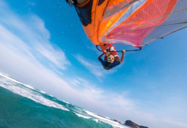 a windsurfer with a bright sail and board does the trick jump in the air over the tropical sea