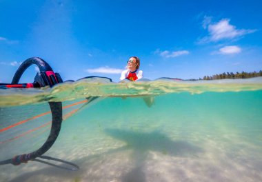 windsurfer girl with a board and a sail in tropical clear water, view from the waterline