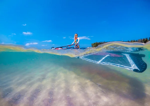 windsurfer girl with a board and a sail in tropical clear water, view from the waterline