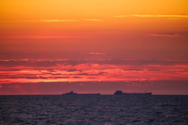 Ufuktaki ticaret gemileri ateşli bir arka planda 