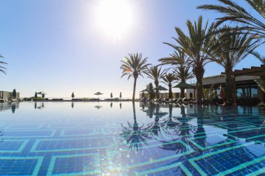 Gün batımında parkta palmiye ağaçları olan bir havuz.