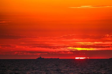 Ufuktaki ticaret gemileri ateşli bir arka planda 