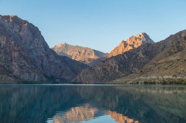 Gün ağarırken Iskanderkul Gölü 'nün ayna yüzeyi dağların arasında.