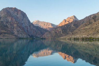 Gün ağarırken Iskanderkul Gölü 'nün ayna yüzeyi dağların arasında.