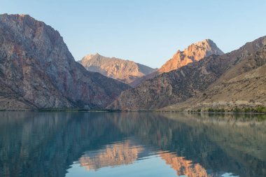 Gün ağarırken Iskanderkul Gölü 'nün ayna yüzeyi dağların arasında.