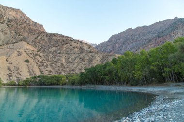 Gün ağarırken Iskanderkul Gölü 'nün ayna yüzeyi dağların arasında.