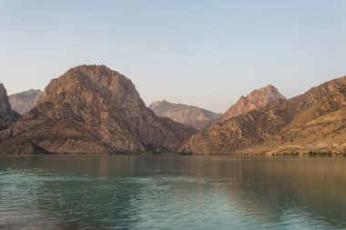 Gün ağarırken Iskanderkul Gölü 'nün ayna yüzeyi dağların arasında.