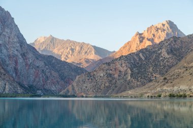 Gün ağarırken Iskanderkul Gölü 'nün ayna yüzeyi dağların arasında.