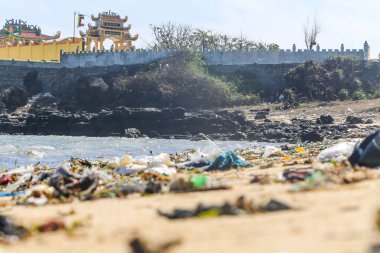 Tropik deniz kıyısındaki Budist tapınağı ve plastik çöplerle dolu kumlu bir plaj. Asya kıtasının kıyılarında ekolojik bir felaket. Kıyı plastiği enkazı dağları