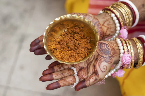 brass bowl of turmeric paste on palm of indian bride