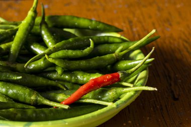 Tabakta yeşil biber ve ahşap masa arasında bir kırmızı biber.