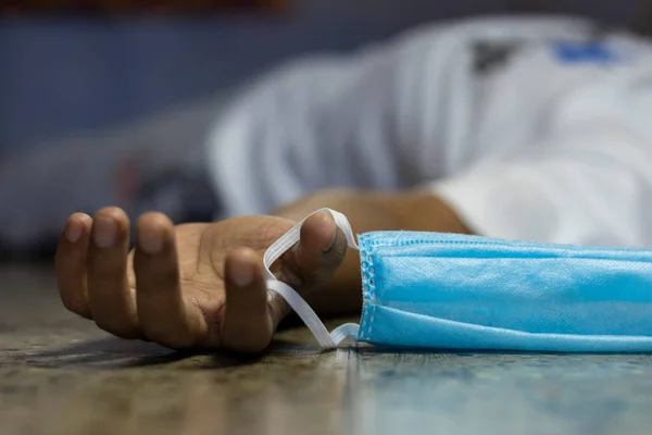 Hintli ya da Asyalı biri COVID-19 ya da korona virüsü salgını sırasında, seçici odaklı ya da sığ alan derinliğinde bir burun maskesi tutarak yerde ölü yatıyor.