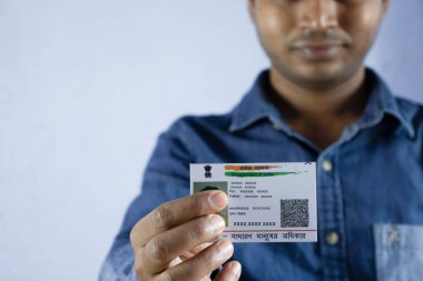 Yüzü gülen bir Hintli beyaz arka planda seçici odaklı ya da sığ bir alan derinliğinde aadhaar kartı tutuyor.