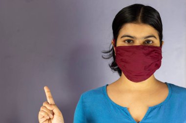 Ev yapımı pamuk burun maskesi takan Hintli bir kadın kameraya bakıyor ve beyaz arka planda Corona virüsü ya da covid-19 koruması için sağ tarafı işaret ediyor.