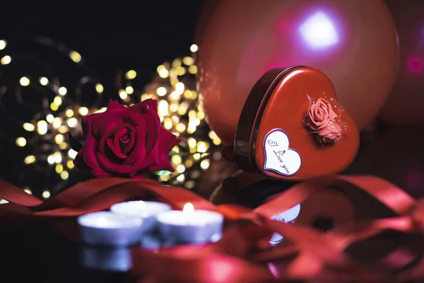 Valentine\'s Day background. Gifts, ribbon, red rose, candles, balloon and confetti on black background with heart shape bokeh lights. Valentines day concept. Flat lay, front view, selective focus, cop