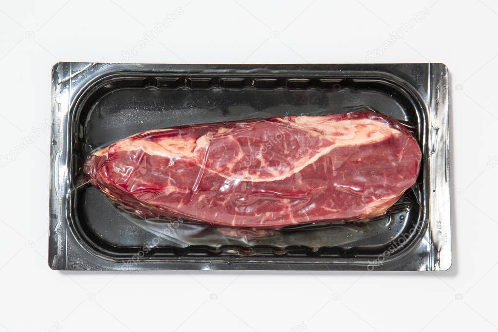 Black plastic pack with fresh beef steak isolated on white background. Raw meat packed without label top view, vacuum packed