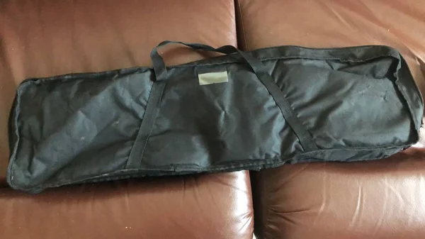 On the couch bag.  Black bag with a lock.  Cover for fishing rods on a brown sofa.  Backpack with handles.  Synthetic fabric in luggage. Leather sofa in the living room.