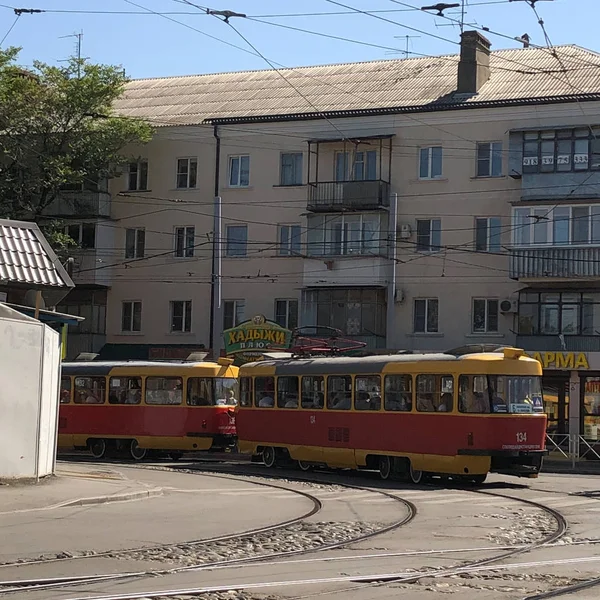 Tramvay rayları, şehirde asfalt, kaldırım, bariyer, taşlar, çakıllar, iki tren, elektrik, ev, beş katlı bina, eski ev, yaz, açık gün, işe yolculuk, toplu taşıma. Balkonlar, kurutma giysileri, acele eden insanlar, yolculuk.