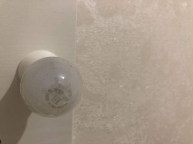 Homeliness, a light on the mirror, a handle on the cabinet, a plug in the socket, black cord, iron handle, the light is on, there is no chandelier, white ceiling, bright interior. A handle with a lock, a wooden door, a torn sofa, a white sofa.