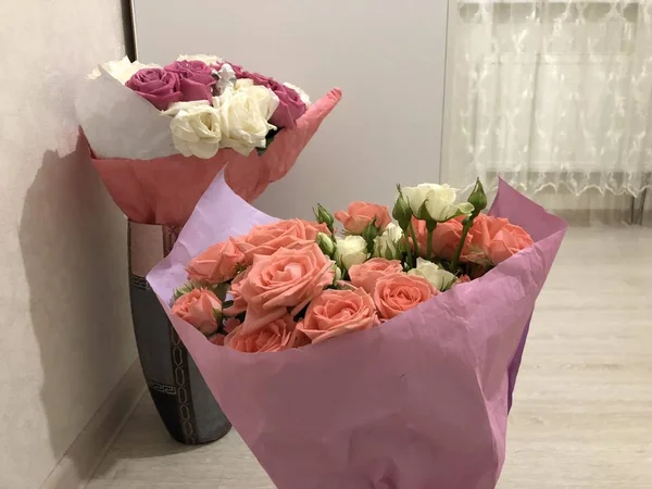 Bouquet of roses.  Pink and white flowers.  Spring bouquet.  Gift to your girlfriend.  Set of flowers for a woman.  Green stems with leaves.  Fresh flowers in paper and a vase.  Plants at home.  White and bright room.  Lovers day.  Happy Valentine\'s