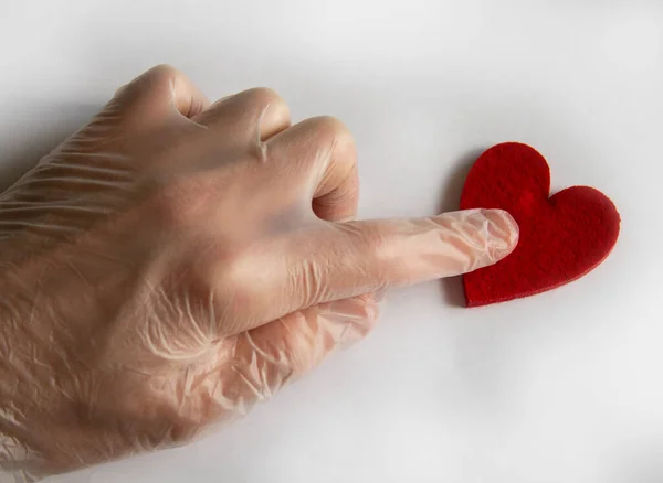 Hand in a transparent glove clicks on a red heart on a white background.