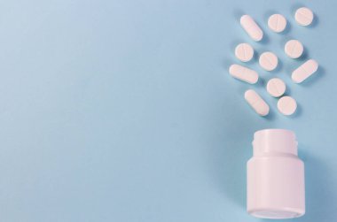 Mavi arka planda bir yığın hap. Beyaz haplar mavi bir arka planda beyaz bir kavanozdan düşüyor. Metin için kopyalanma alanı.