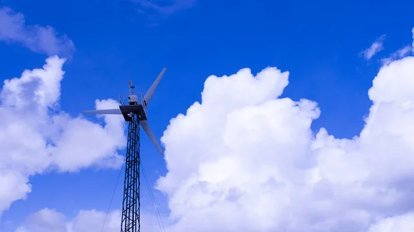 Küçük gri bir rüzgar jeneratörü bulutlu mavi gökyüzüne karşı alternatif rüzgar enerjisi üretir..