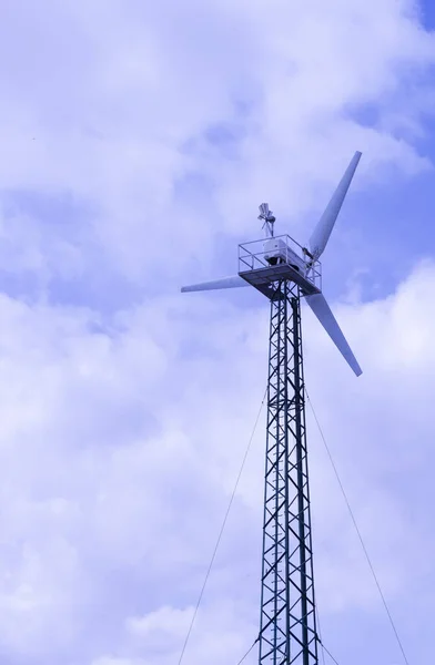 a wind turbine generates electrical energy against a cloudy blue sky. Vertical photo.