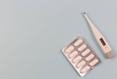 Kabarcık paketlerinde beyaz tabletler ve mavi arka planda elektronik termometre. En üst noktadan fotoğraf. Nesneler kenarda. Metin için kopyalama uzayı